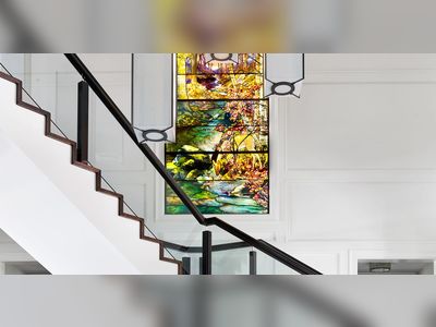 a tiffany studios landscape window overlooks a staircase with glass balustrade and a round glass topped table in foreground